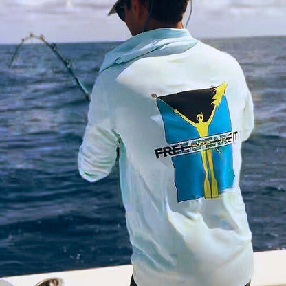 Action shot of an angler wearing the Free Spear-It Bahamas Bounty Long Sleeve UPF 50+ Solar Hoodie in light blue while reeling in a catch on the open ocean. The back of the shirt showcases the bold Bahamas-inspired logo design, featuring a freediver holding a speared hogfish and the Bahamian flag. Ideal for sun protection and comfort during fishing and outdoor adventures.