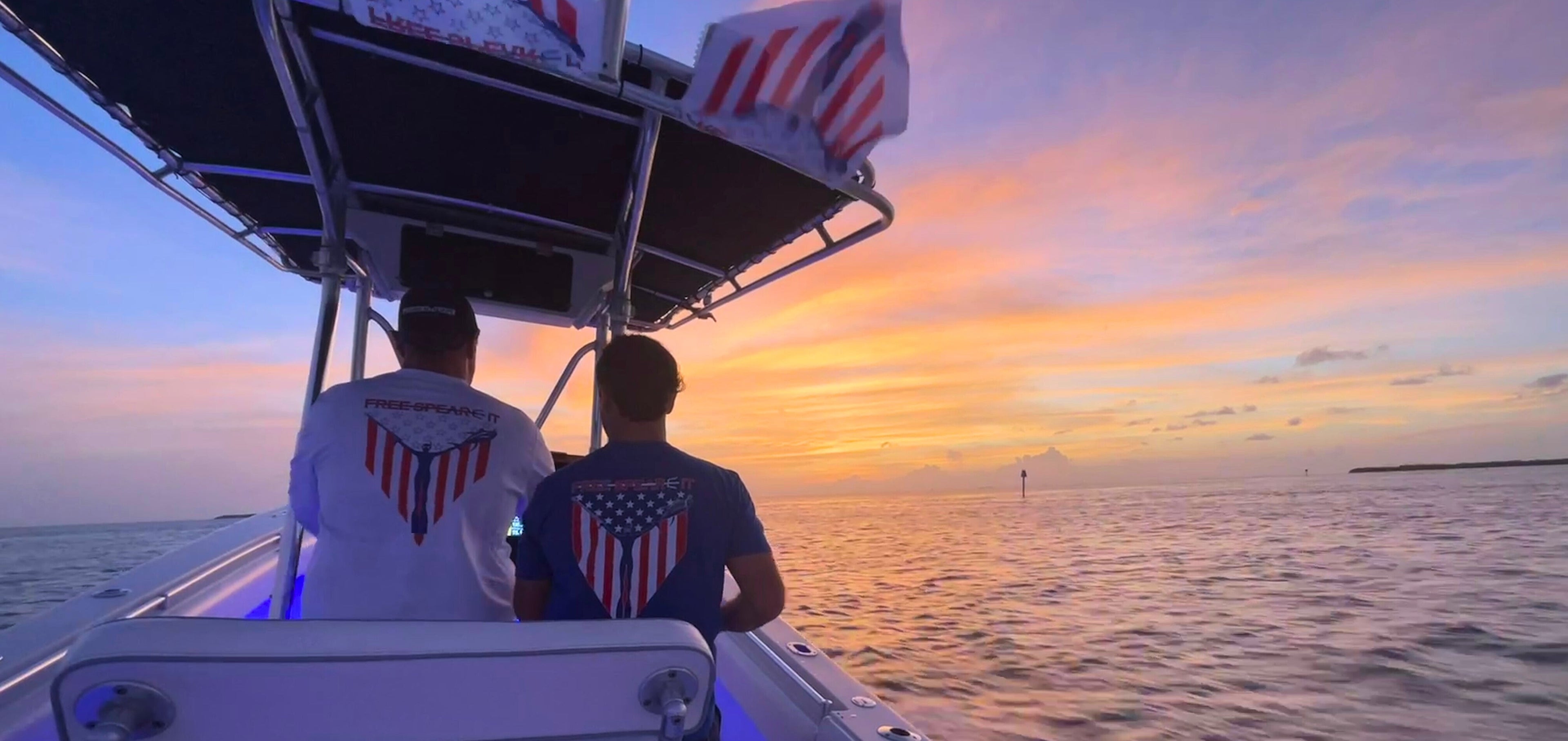 Two freedive spearfishers wearing Free Spear-It's Spear-It of Freedom patriotic shirts on a boat at sunset in the USA