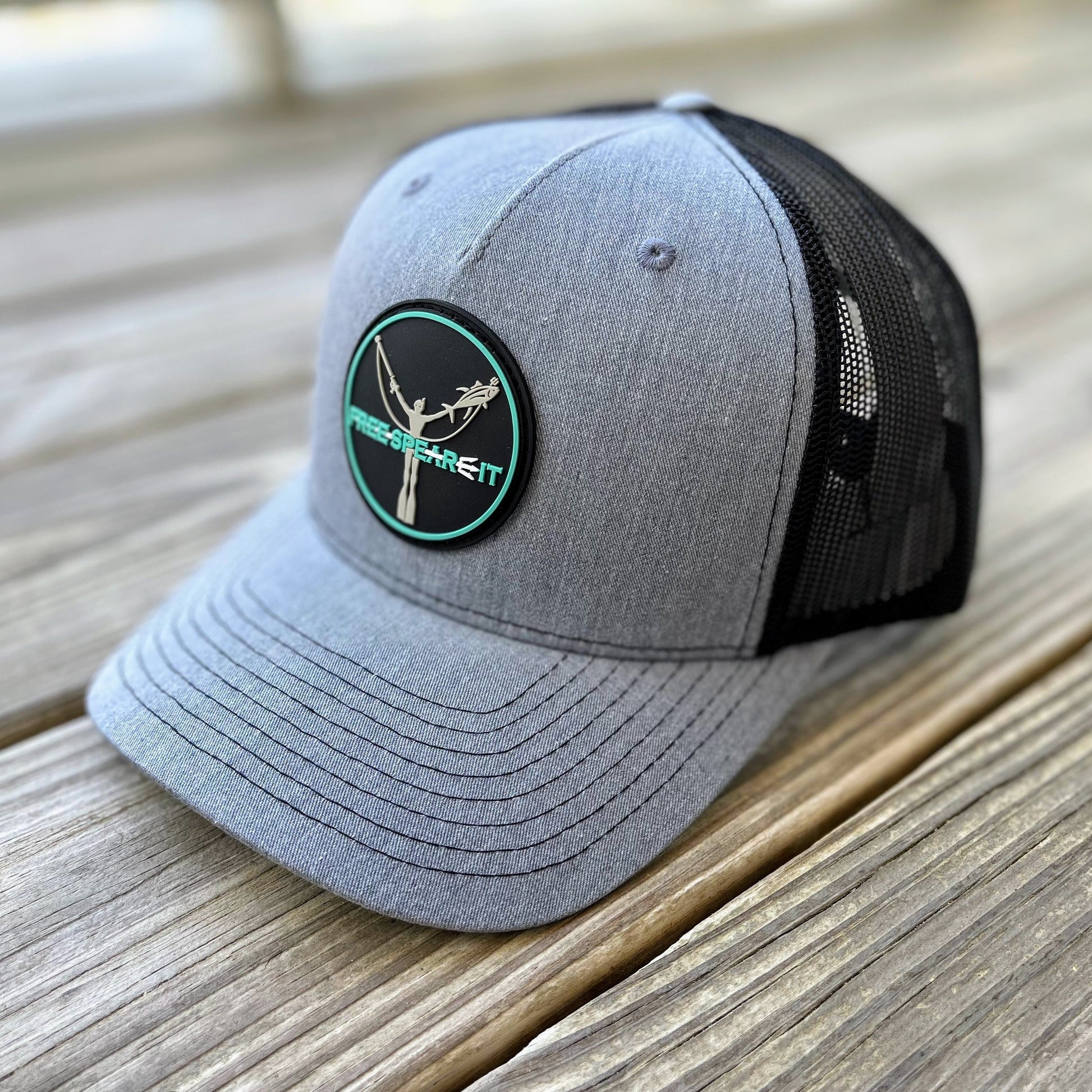 Close-up of the Free Spear-It PVC Logo Snapback Hat in heather grey and black, featuring a durable PVC rubber patch with a freediver and speargun design. This Richardson trucker hat blends comfort and performance, perfect for spearfishing, boating, and everyday wear.